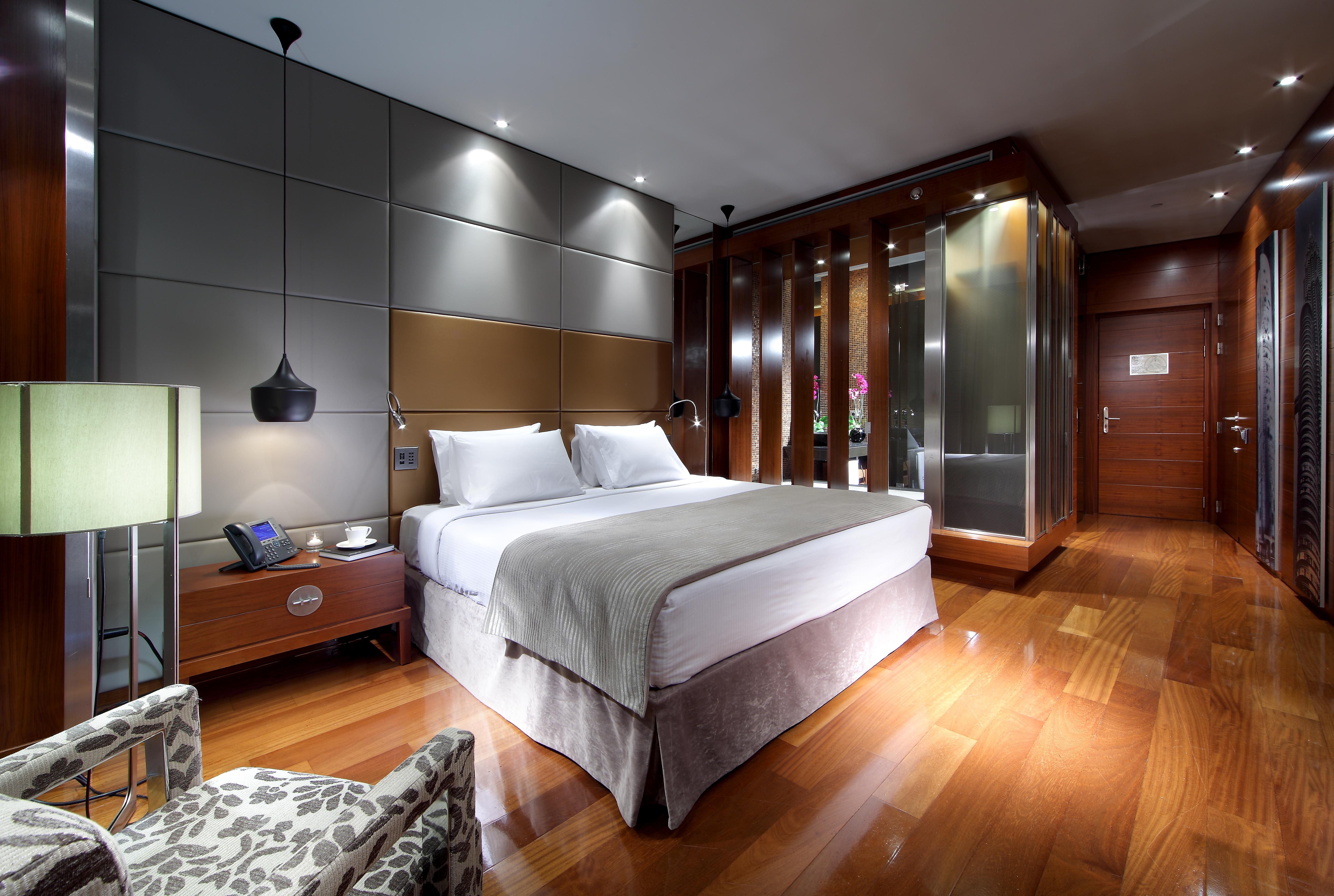 유로스타 마드리드 타워 외부 사진 The photo shows a modern hotel room featuring a double bed dressed in white linens with a light gray blanket. Beside the bed, there is a stylish nightstand with a lamp and a phone. The room has a sleek design with wooden flooring and contemporary dec