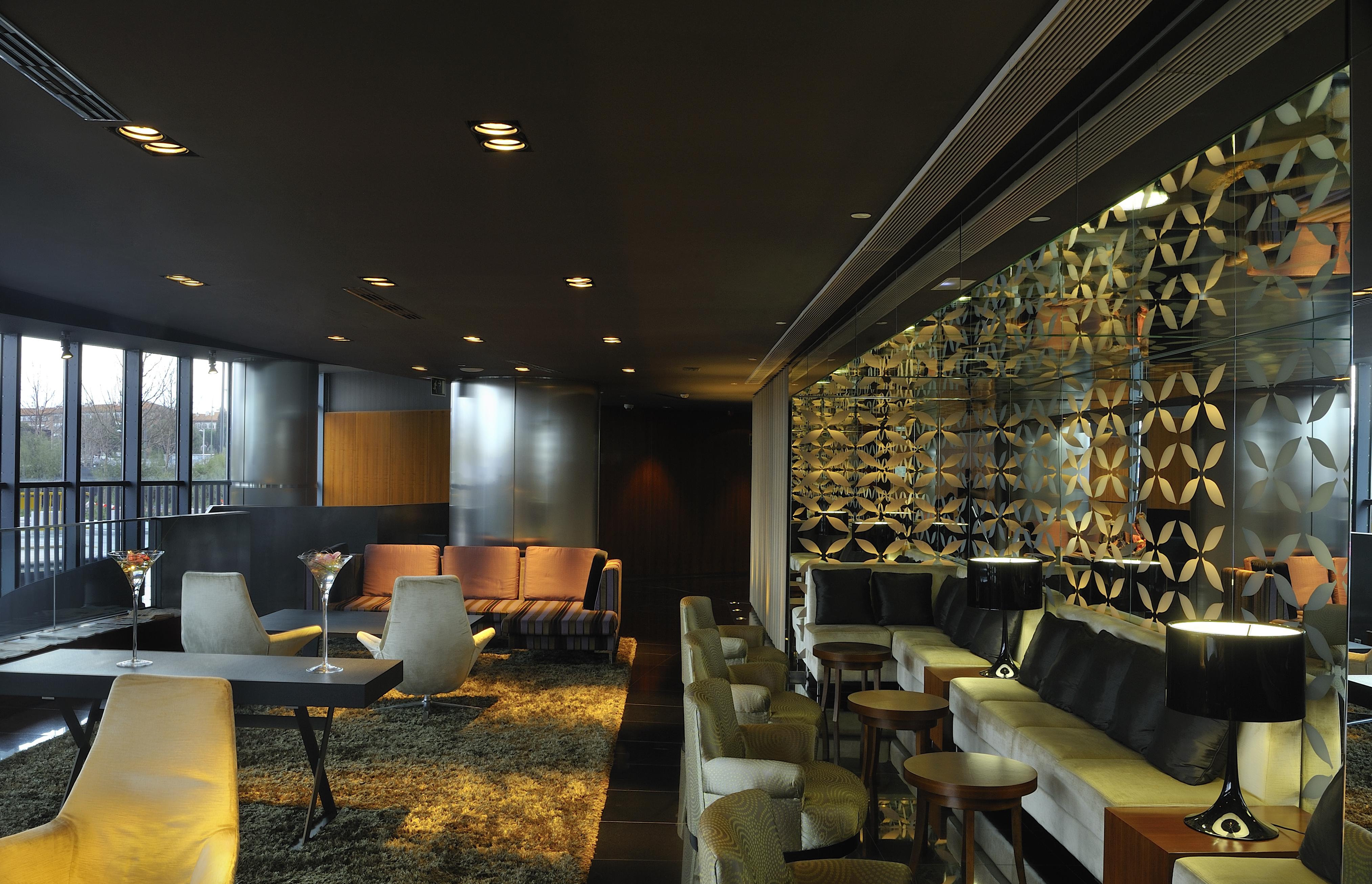 유로스타 마드리드 타워 외부 사진 The photo shows a contemporary and stylish interior space, likely a lounge or bar. The design features a mix of seating arrangements, including plush chairs and modern sofas, set against a dark backdrop with soft lighting. A decorative wall with an i