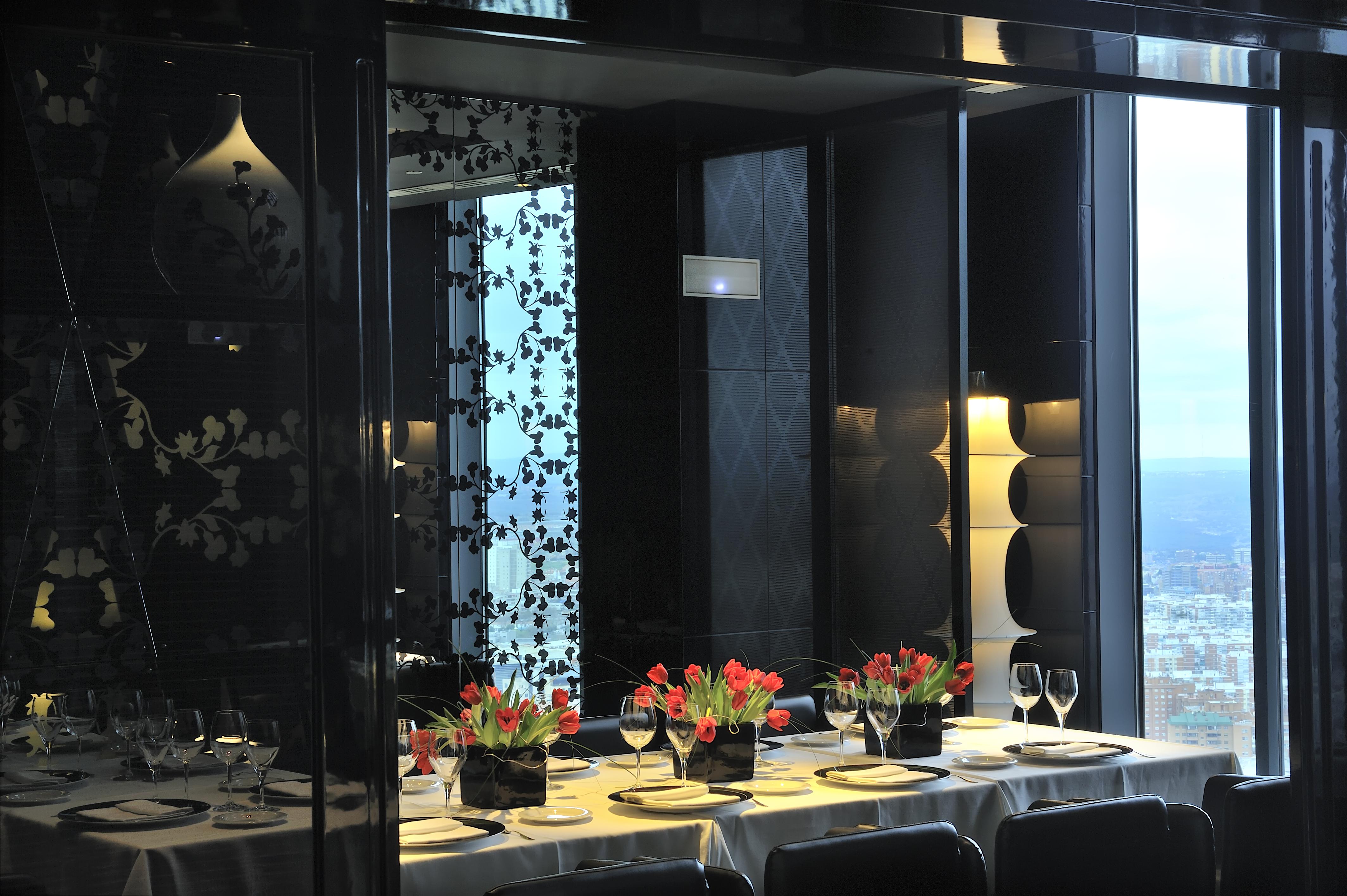 유로스타 마드리드 타워 외부 사진 The photo shows a stylishly decorated dining area with a long table set for a meal. The table is adorned with elegant plates, glasses, and small vases of vibrant tulips as centerpieces. The interior design features a mix of dark and light elements, w