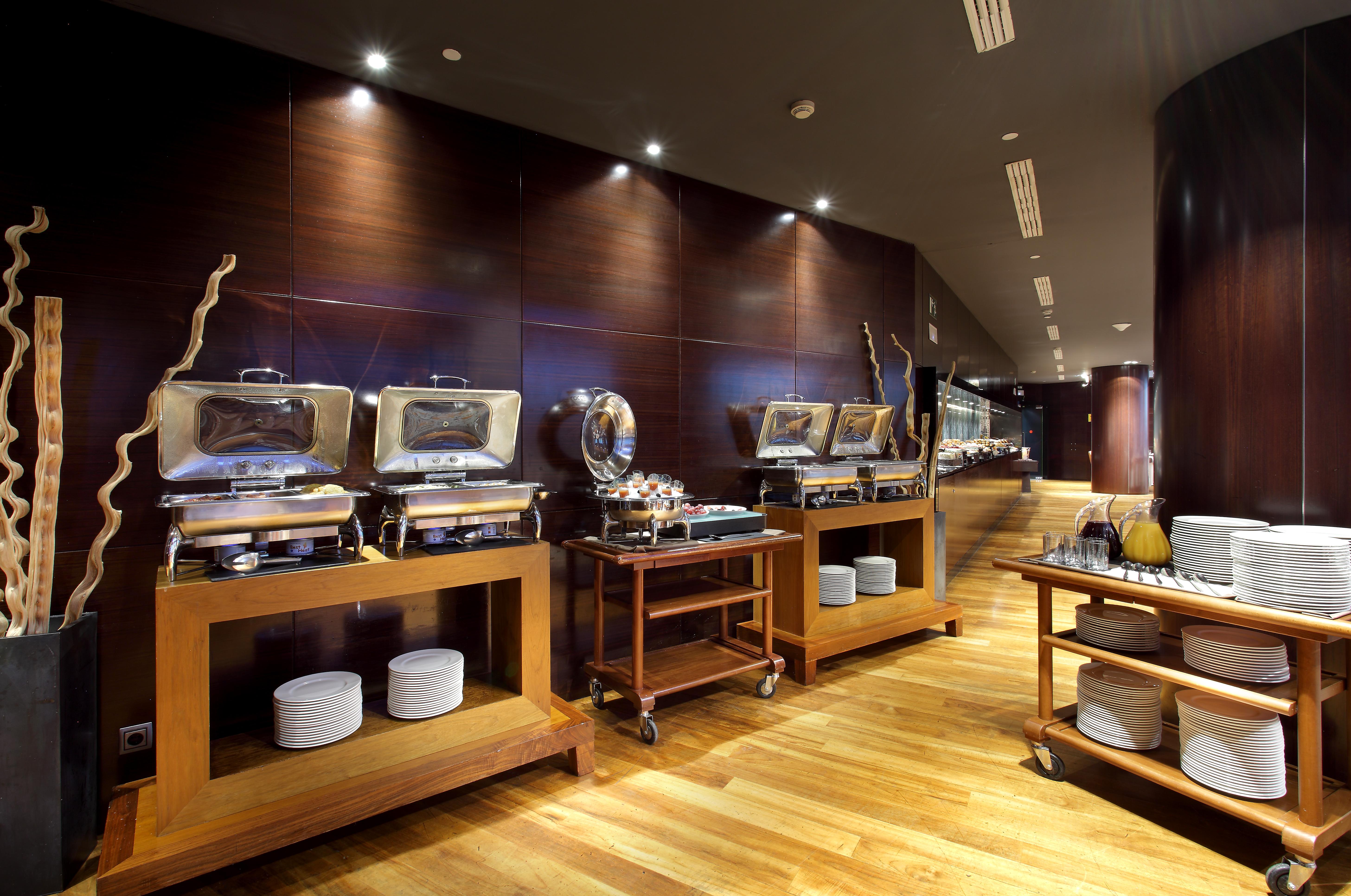 유로스타 마드리드 타워 외부 사진 The photo shows a modern restaurant buffet setting. There are several food warmers placed on wooden tables, showcasing a variety of dishes. The walls have a dark wood finish, and the lighting is soft and ambient, creating an elegant atmosphere. In fr