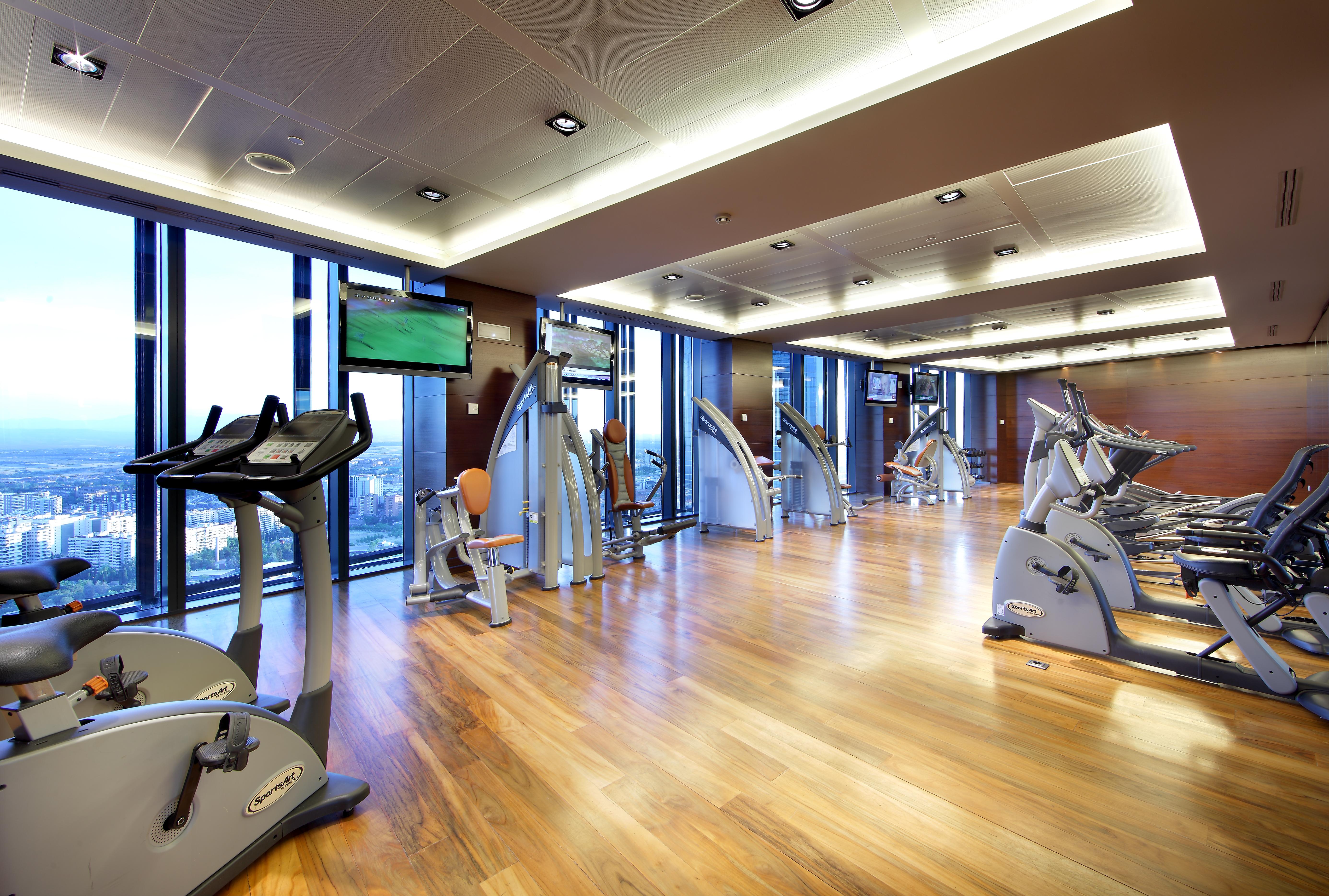 유로스타 마드리드 타워 외부 사진 The photo shows a modern gym or fitness center. It features large windows that let in natural light, providing a view of the outside. The flooring is made of polished wood, giving the space a warm and inviting atmosphere. Various exercise machines ar