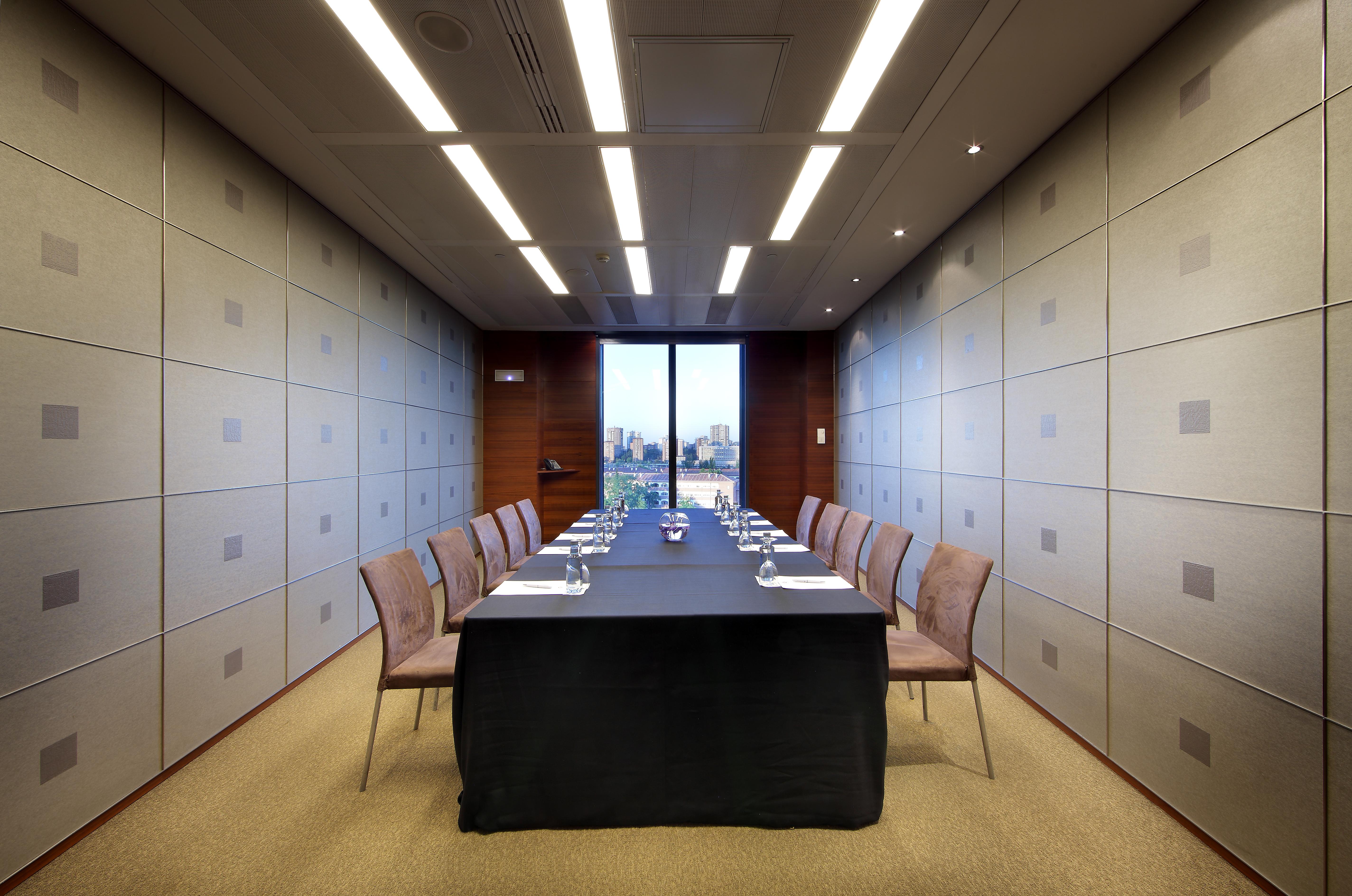유로스타 마드리드 타워 외부 사진 The photo shows a modern conference room. In the center, there is a long table covered with a black tablecloth. Surrounding the table are several chairs arranged neatly. The walls have a sleek design with light-colored panels, and overhead, there are