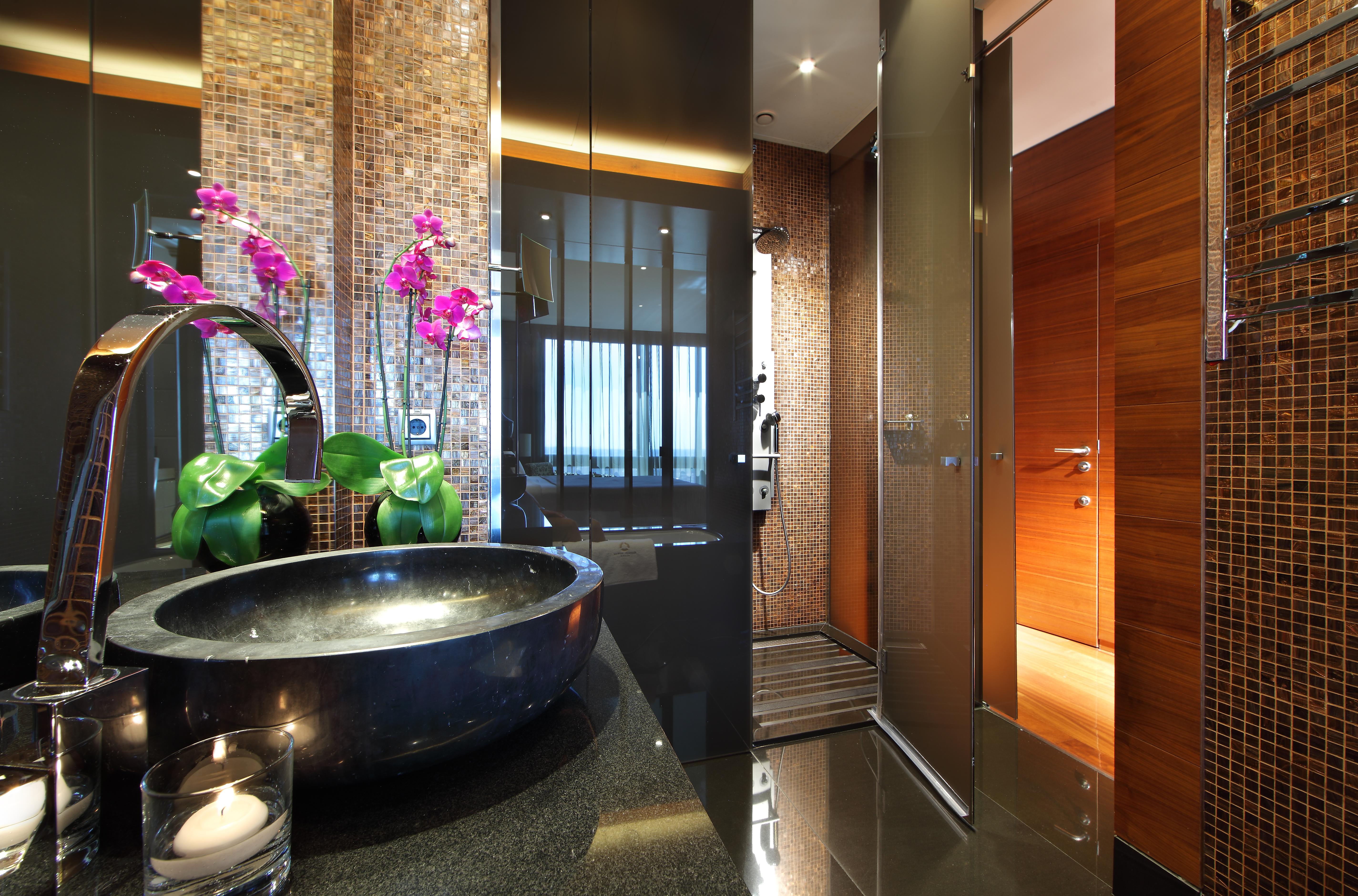 유로스타 마드리드 타워 외부 사진 The photo shows a modern and stylish bathroom. On the left, there is a sleek black basin set on a dark countertop, adorned with decorative elements such as a candle and potted green plants. To the side, there are elegant pink orchids adding a pop of 