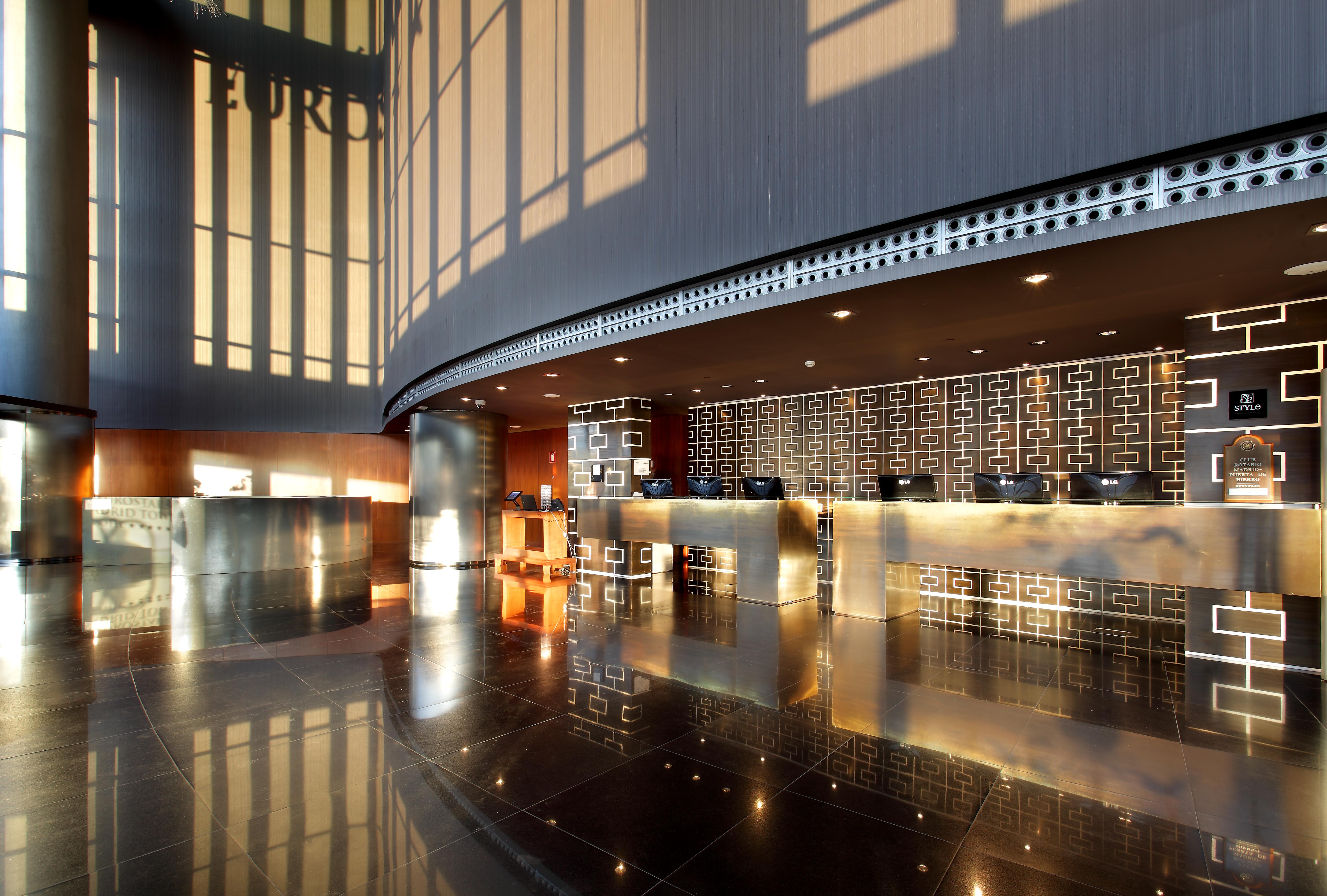 유로스타 마드리드 타워 외부 사진 The photo shows the interior of a modern hotel lobby. It features a sleek reception desk with a polished surface and an elegant design. The lobby has large windows allowing natural light to flood in, creating a bright and inviting atmosphere. The flo