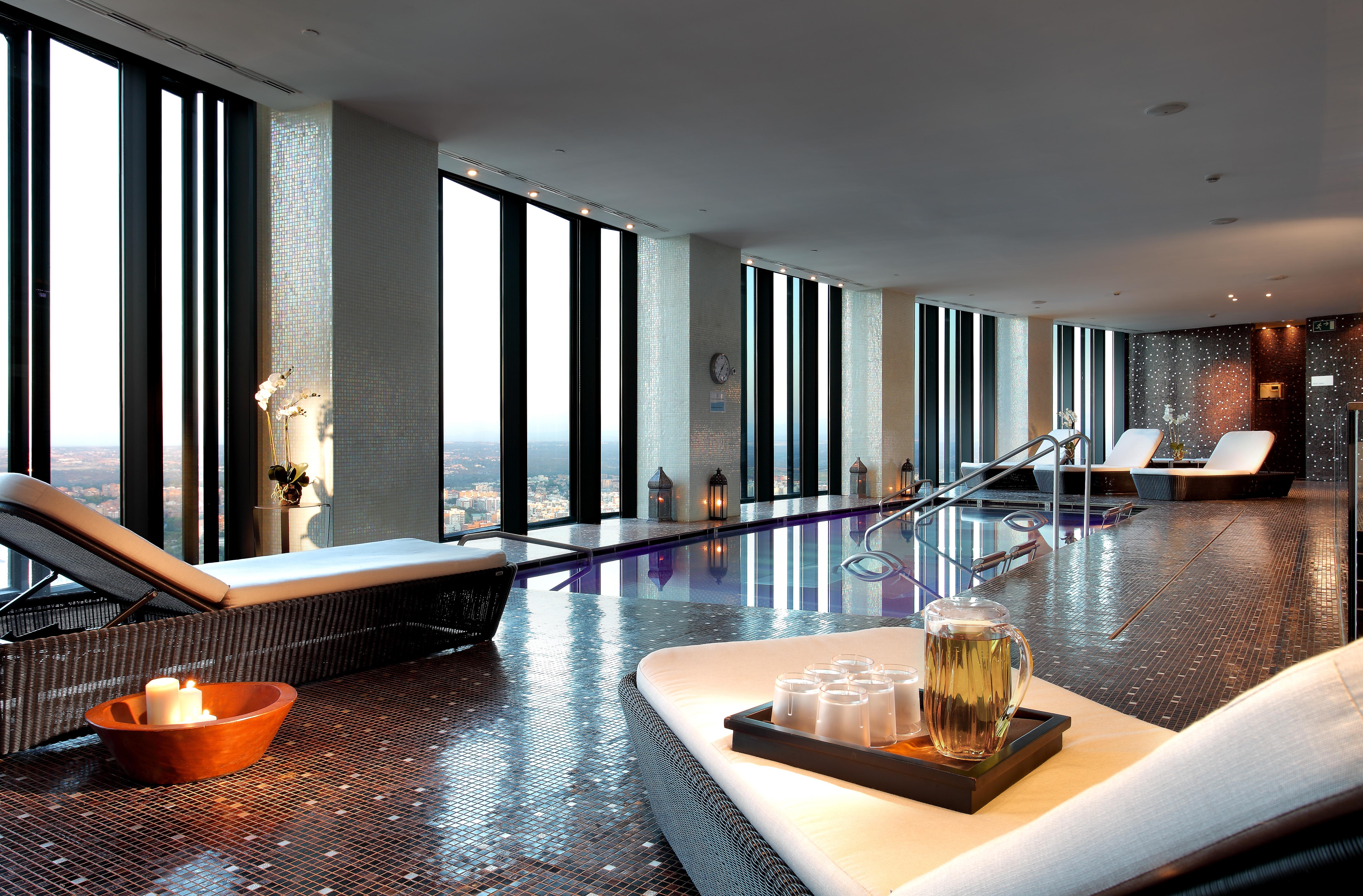 유로스타 마드리드 타워 외부 사진 The photo depicts a luxurious spa interior with large windows that offer a panoramic view of the outside. The space features sleek, modern lounge chairs and a tranquil atmosphere. There is a pool area, and the floor is tiled with reflective materials