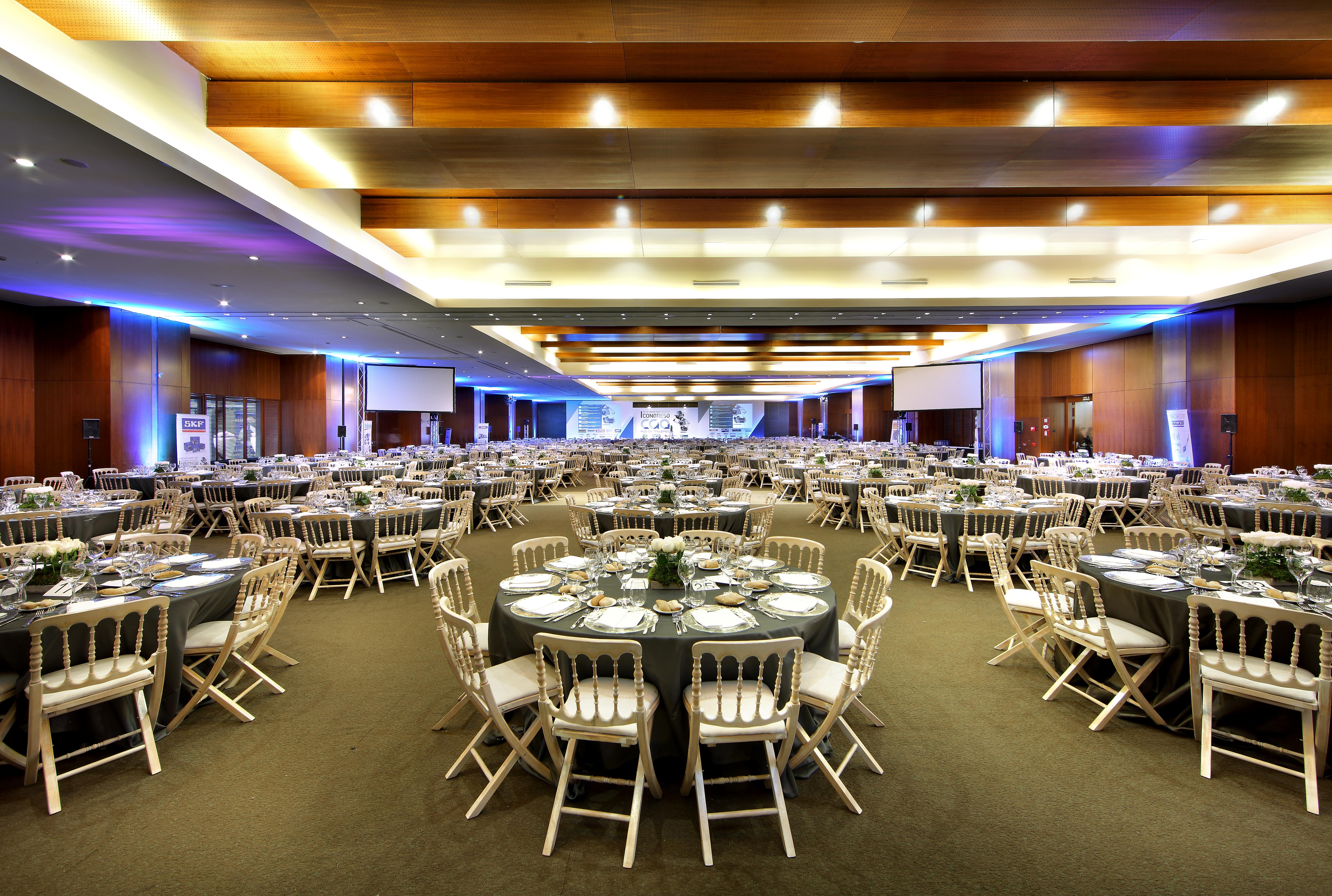 유로스타 마드리드 타워 외부 사진 The photo shows a large banquet hall set up for an event. The room is filled with numerous round tables, each adorned with dark tablecloths and decorative centerpieces. There are white chairs arranged around the tables. The lighting is soft, with a c