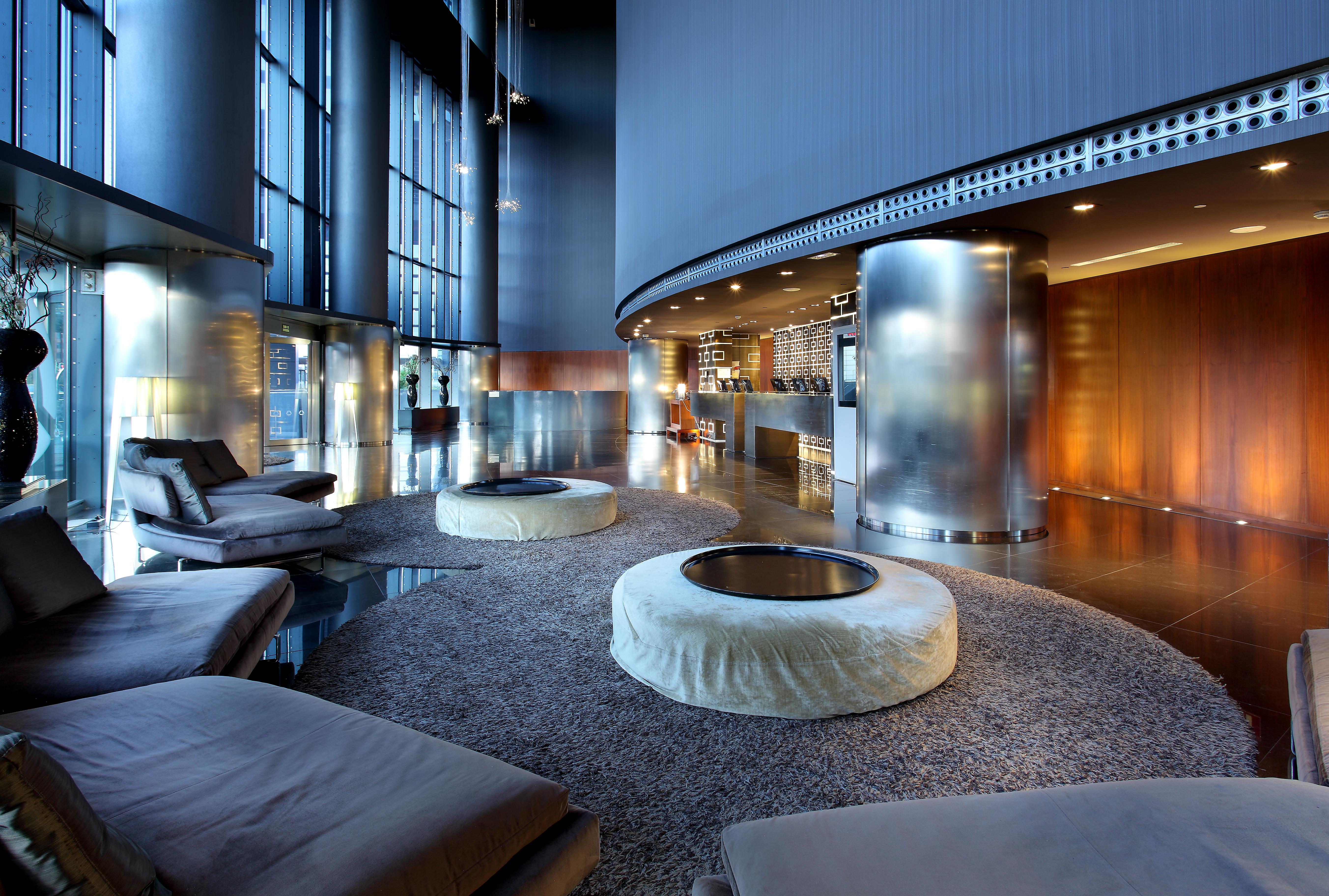 유로스타 마드리드 타워 외부 사진 The photo depicts a modern and stylish lounge area. The space features light-filled windows that allow for ample natural light, creating an airy atmosphere. There are several circular seating arrangements with plush, low-slung cushions arranged aroun