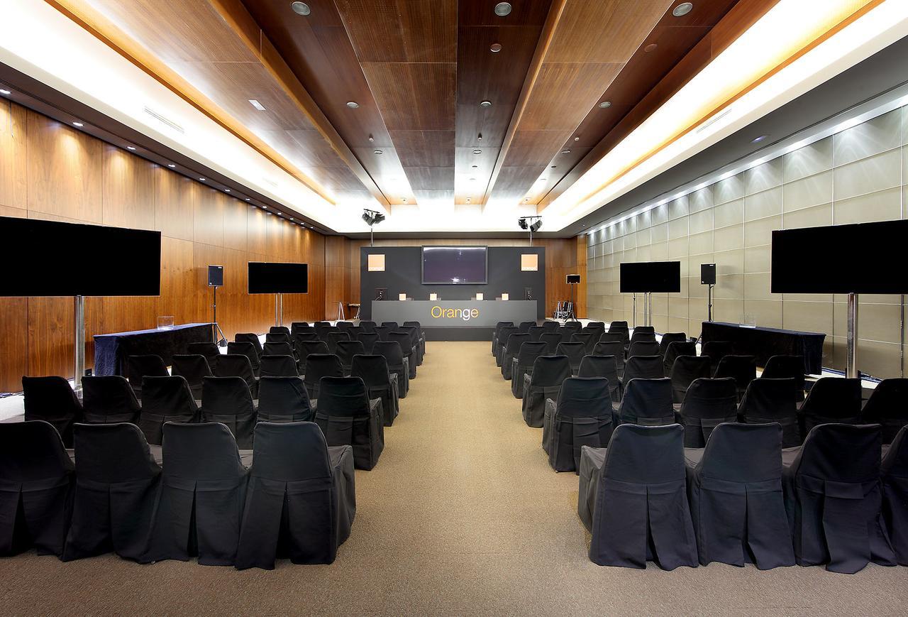 유로스타 마드리드 타워 외부 사진 The photo shows a conference room set up for an event. It features rows of black chairs arranged facing a central stage or podium area. There are large screens on either side of the room, suggesting that presentations or visual displays may be part o