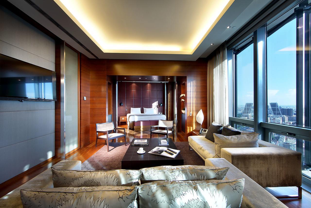 유로스타 마드리드 타워 외부 사진 The photo shows a luxurious hotel room or suite with a modern design. It features large windows that offer a view of the outside, letting in plenty of natural light. The interior has warm wooden accents on the walls and sophisticated lighting through