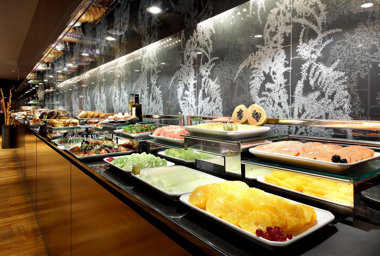 유로스타 마드리드 타워 외부 사진 The photo shows a buffet display featuring a variety of dishes and ingredients. There are plates filled with different types of food, including seafood, fruits, and vegetables. The arrangement is visually appealing, with the food presented on glass s