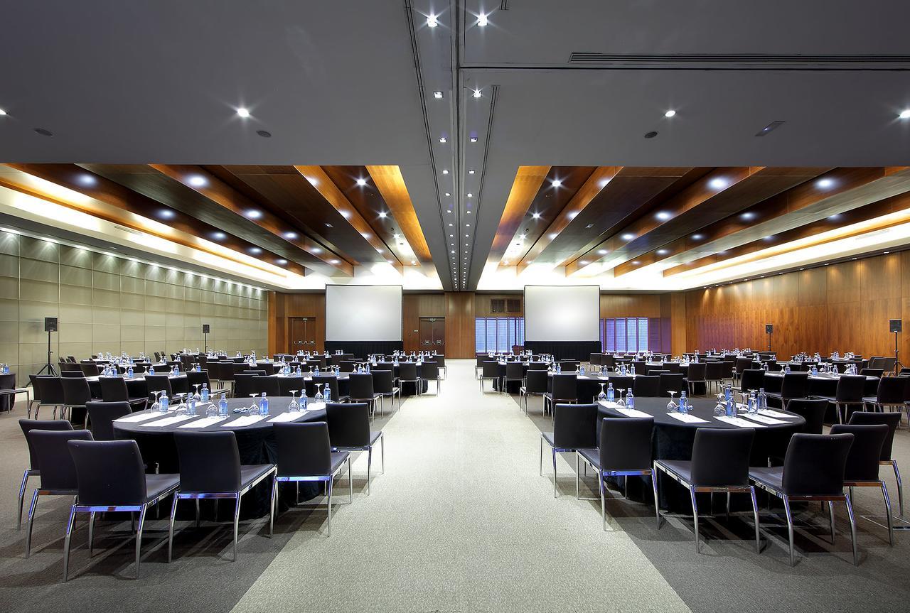 유로스타 마드리드 타워 외부 사진 The photo shows a large conference or meeting room. It features multiple round tables set with chairs arranged around them, indicating that it is prepared for a formal gathering or event. Each table has water bottles and possibly notepads, suggesting