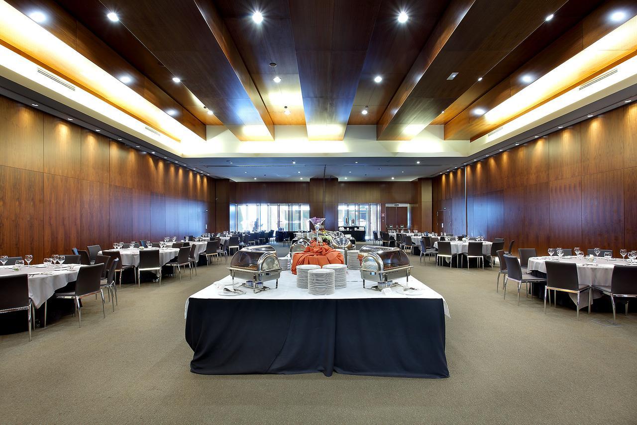 유로스타 마드리드 타워 외부 사진 The photo shows a spacious banquet hall or dining area with a modern design. The room features wooden walls and a high ceiling with lighting that creates a warm ambiance. In the center, there is a large table draped in black cloth, adorned with food 