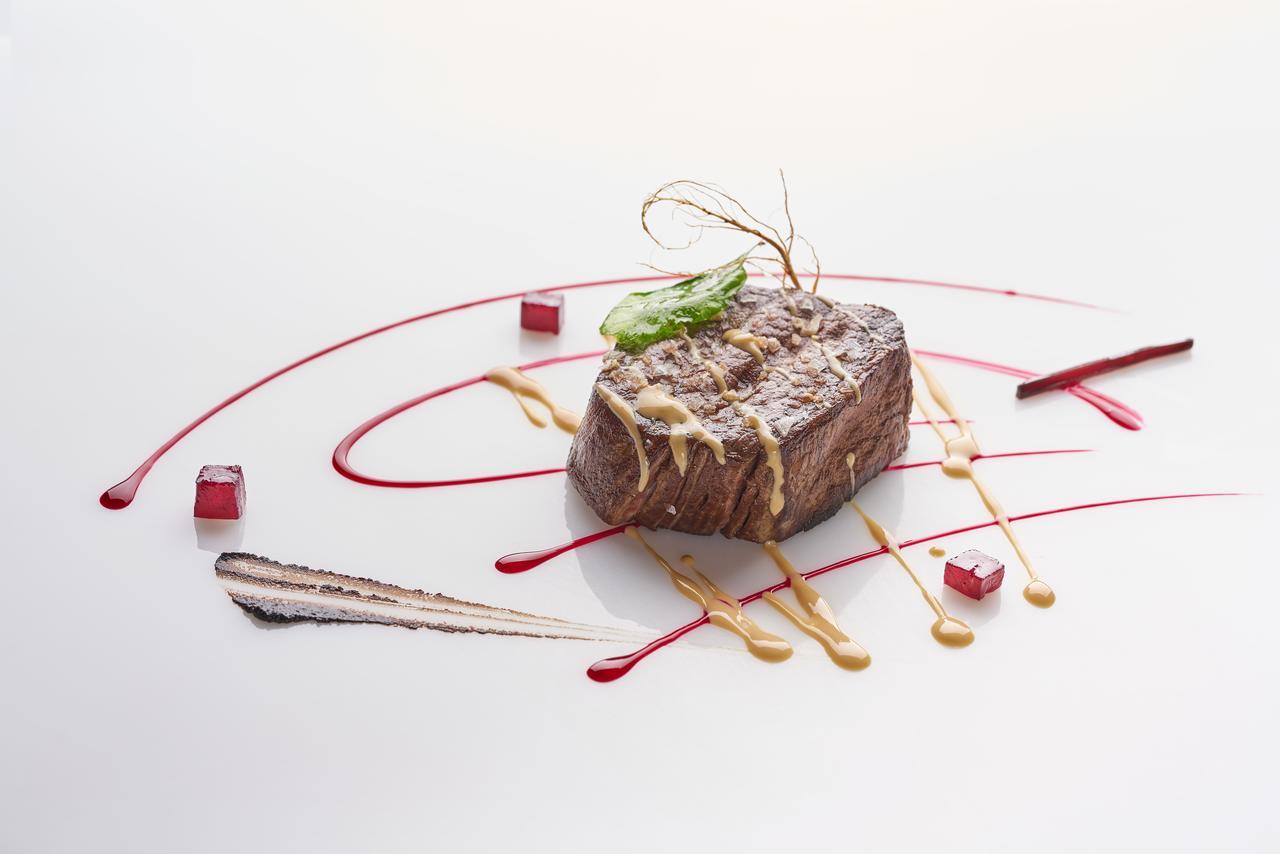유로스타 마드리드 타워 외부 사진 The photo features a beautifully plated dish that showcases a piece of meat, likely a steak, at the center. The meat is glazed with a sauce and garnished with a thin piece of green herb. Surrounding the meat are artistic drizzles of different sauces,