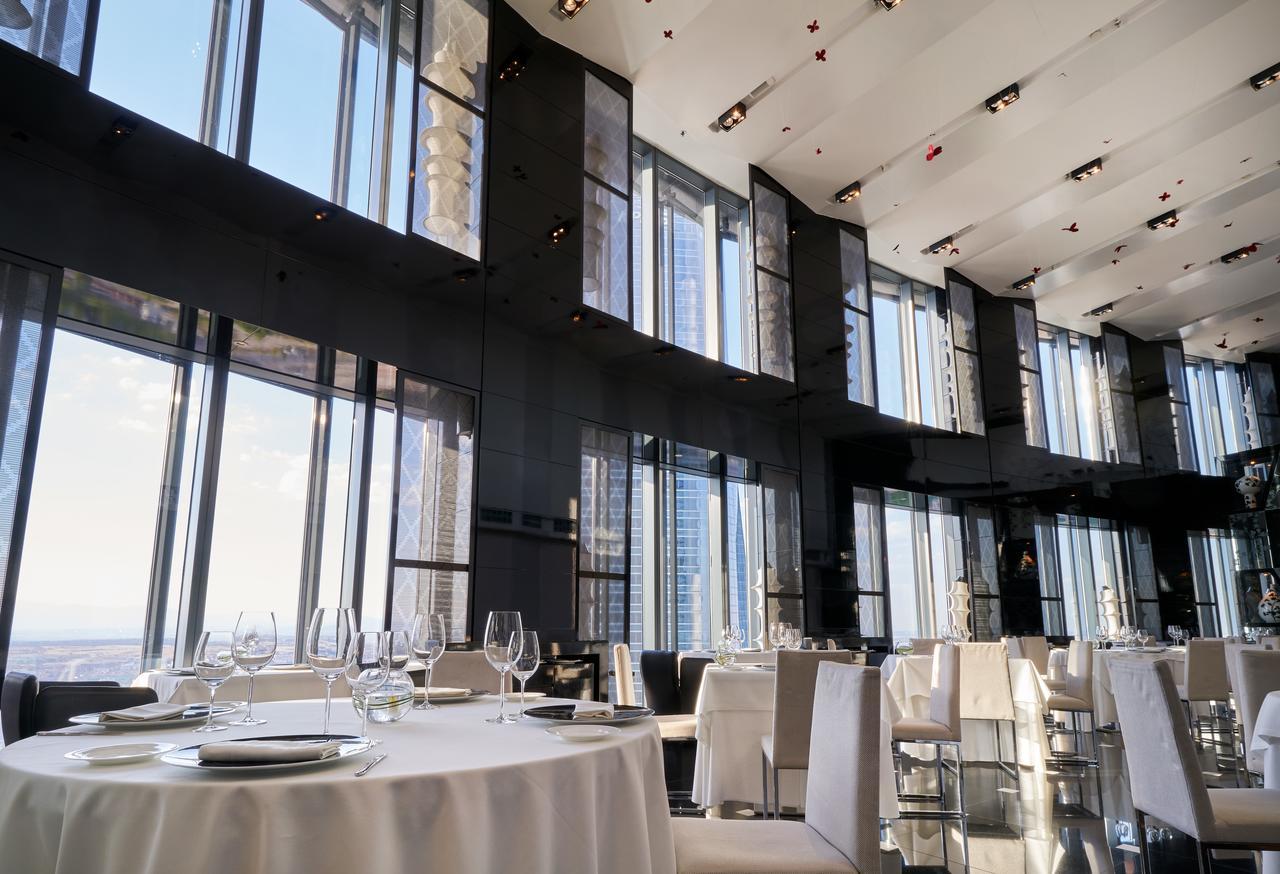 유로스타 마드리드 타워 외부 사진 The photo depicts an elegant restaurant interior characterized by sleek, modern design. It features large floor-to-ceiling windows that allow abundant natural light to fill the space and provide a panoramic view of the outside. The dining area includ