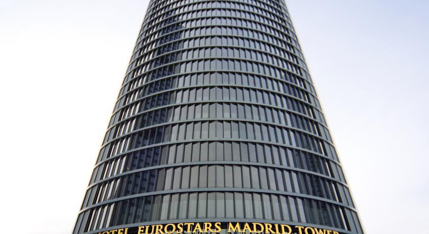 유로스타 마드리드 타워 외부 사진 The photo displays a tall, modern skyscraper known as the Eurostars Madrid Tower. The building features a sleek, glass facade with a cylindrical design. At the base, there's a prominent sign indicating the name of the hotel, “Eurostars Madrid Tower,”