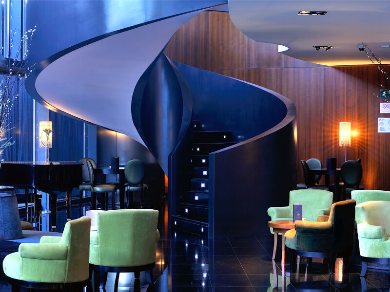 유로스타 마드리드 타워 외부 사진 The photo depicts a stylish and modern interior, likely of a bar or lounge. The focal point is a unique spiral staircase that has a sleek, flowing design, leading to another level. The surrounding area features a combination of dark wood panels and g